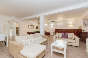 Uma sala de estar ampla com mesa de bilhar, dois sofás, uma mesa de centro e um espaço para refeições.