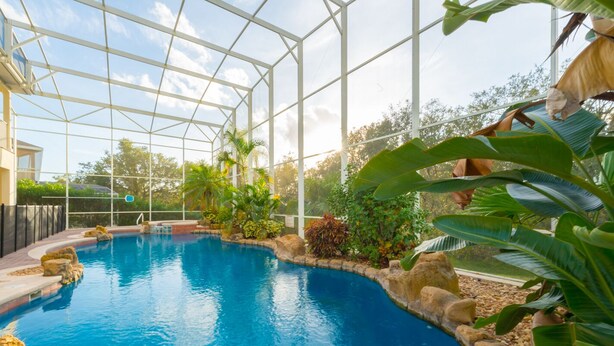 Una piscina con agua azul cristalina, rodeada de rocas y plantas tropicales, dentro de una estructura de vidrio.