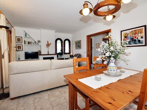 Una sala de estar con sofá, mesa de comedor de madera, sillas, televisor y chimenea.