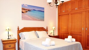 Un dormitorio con una cama de madera, dos mesitas de noche con lámparas, un armario grande y una pintura con vista al mar.