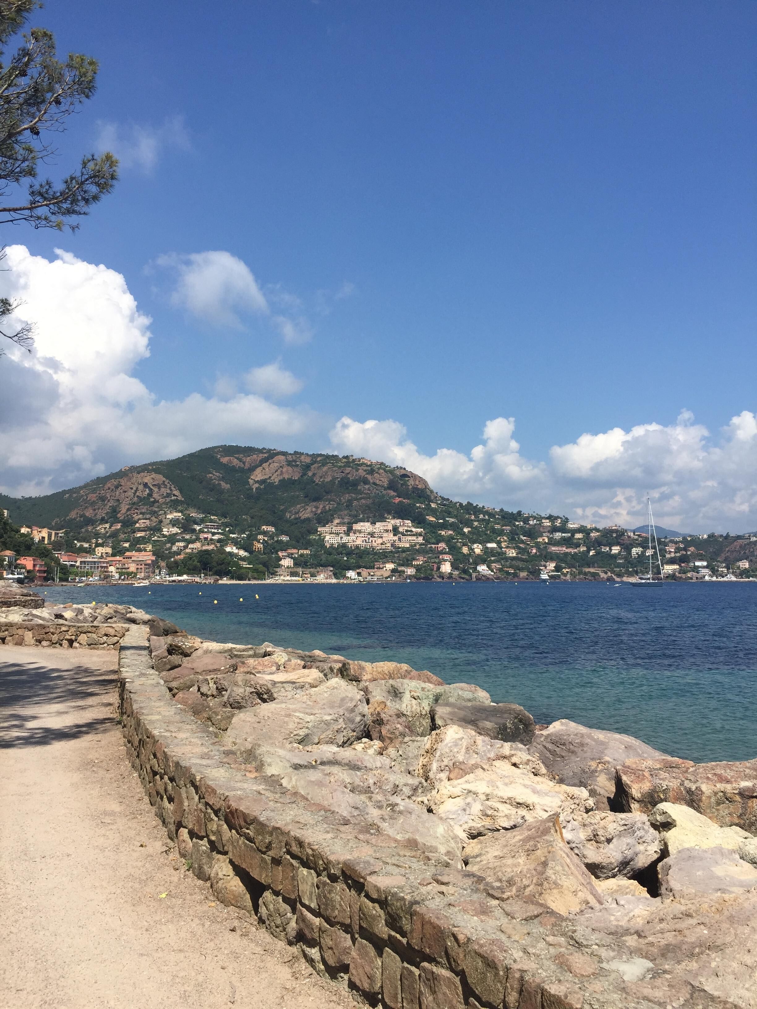 A coastal view with a stone wall, clear blue sky, and a distant town with buildings.