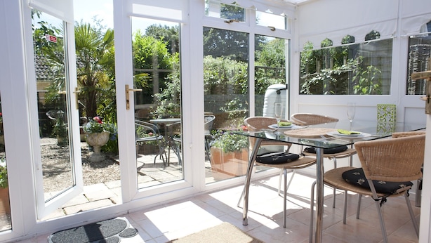 A conservatory with a glass table and chairs, surrounded by potted plants and a view of the garden. - Little Chequers is a pretty pet friendly cottage , sleeps 3. close to Aldeburgh (Friston)
