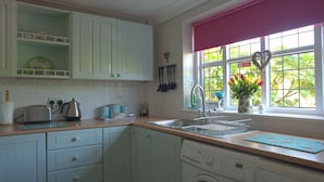 A kitchen with white cabinets, a washing machine, a sink, and a window with a view of greenery. - Little Chequers is a pretty pet friendly cottage , sleeps 3. close to Aldeburgh (Friston)