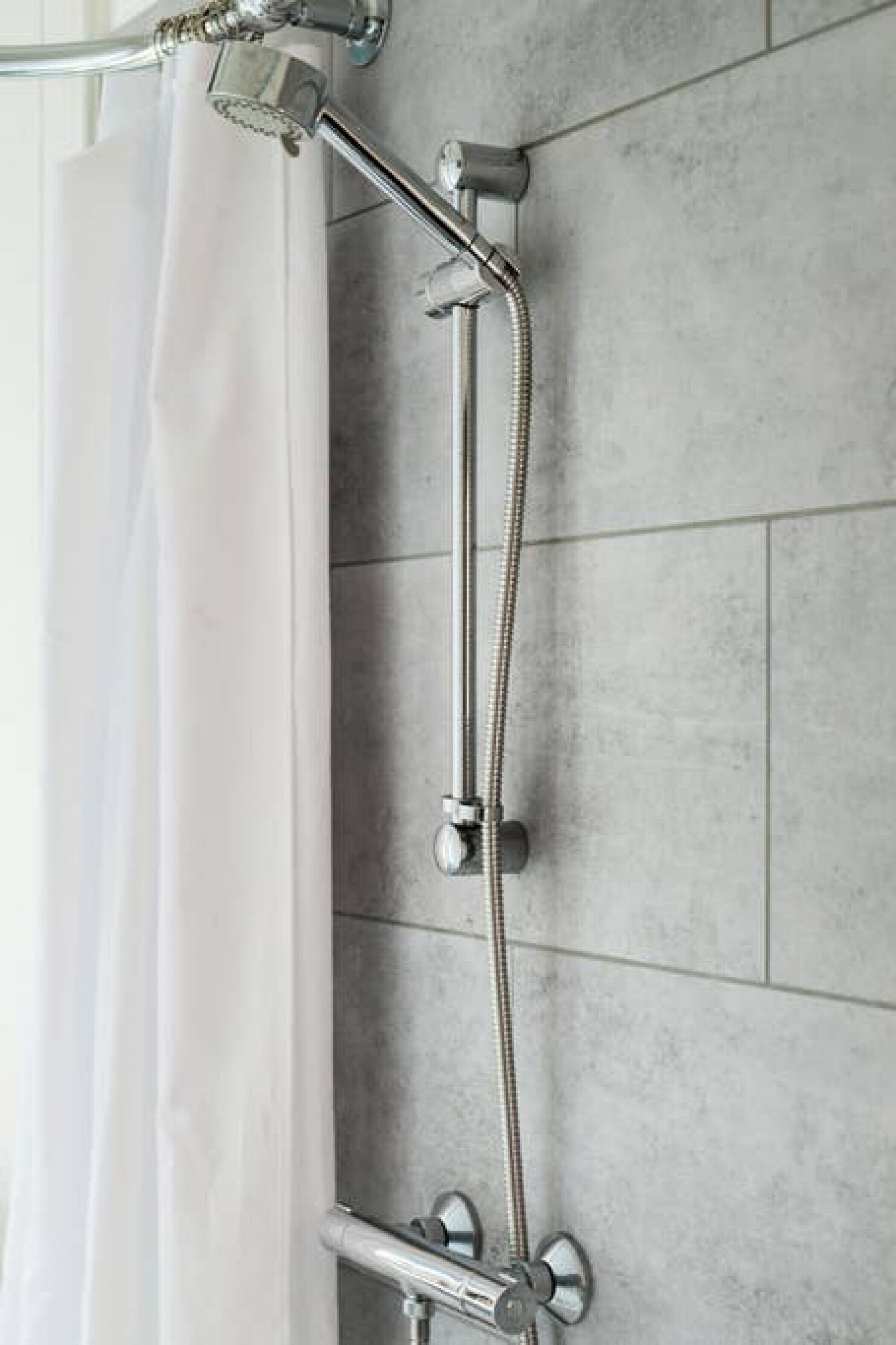 Une douche équipée d’un pommeau de douche à main et d’un pommeau de douche fixe, tous deux fixés sur un mur dont la surface est recouverte de carreaux.
