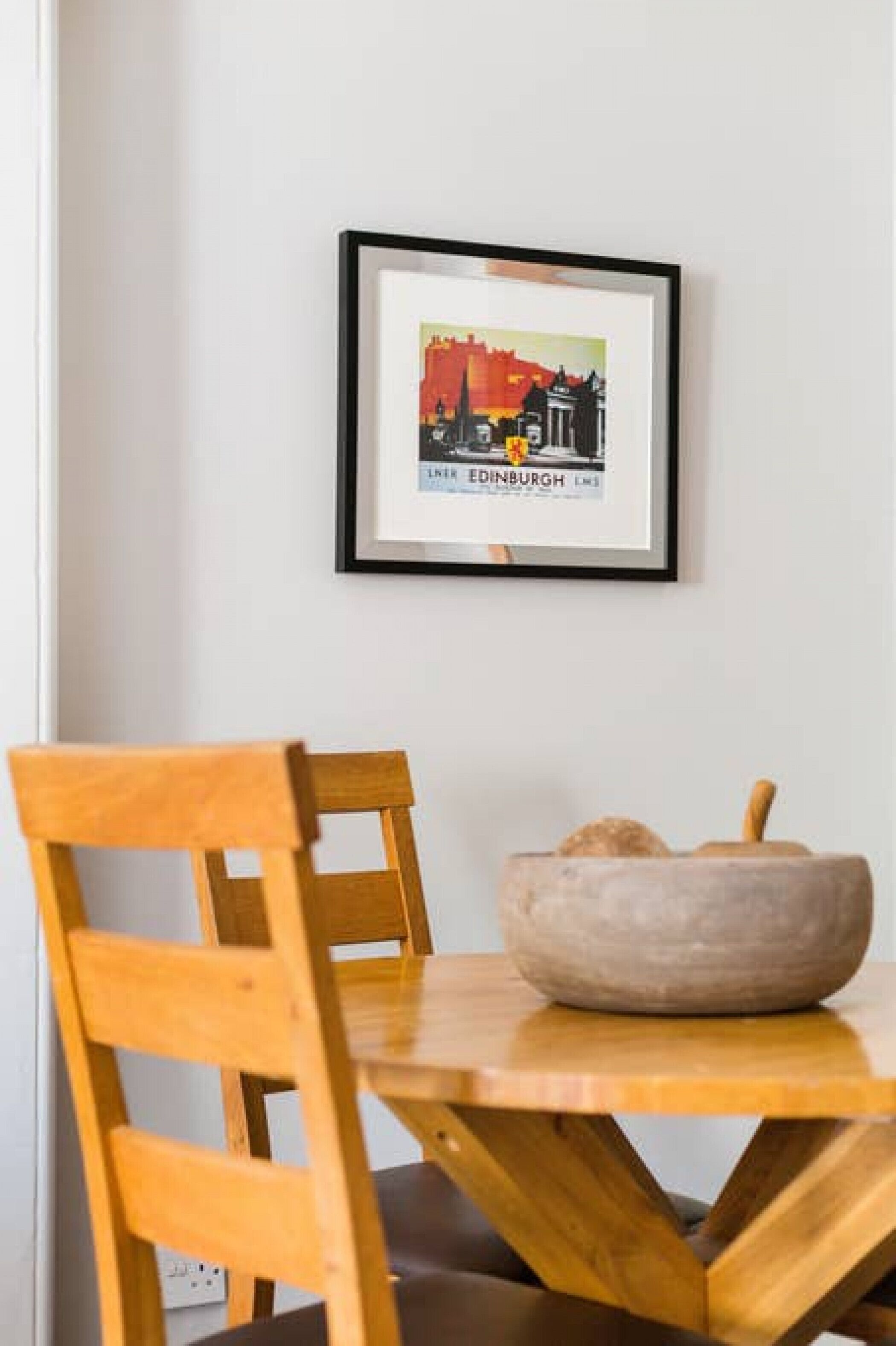 Un tableau encadré représentant Édimbourg est accroché au mur, une chaise en bois et un bol en pierre sont posés sur une table.