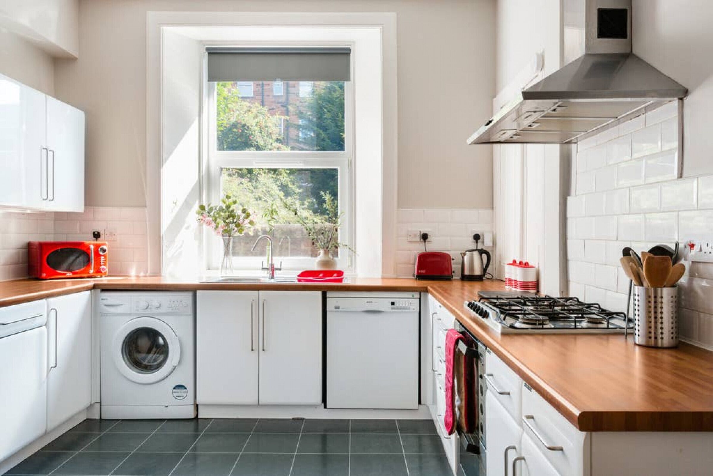 A modern kitchen with white cabinetry, a built-in washing machine, a red microwave, and a gas stove.