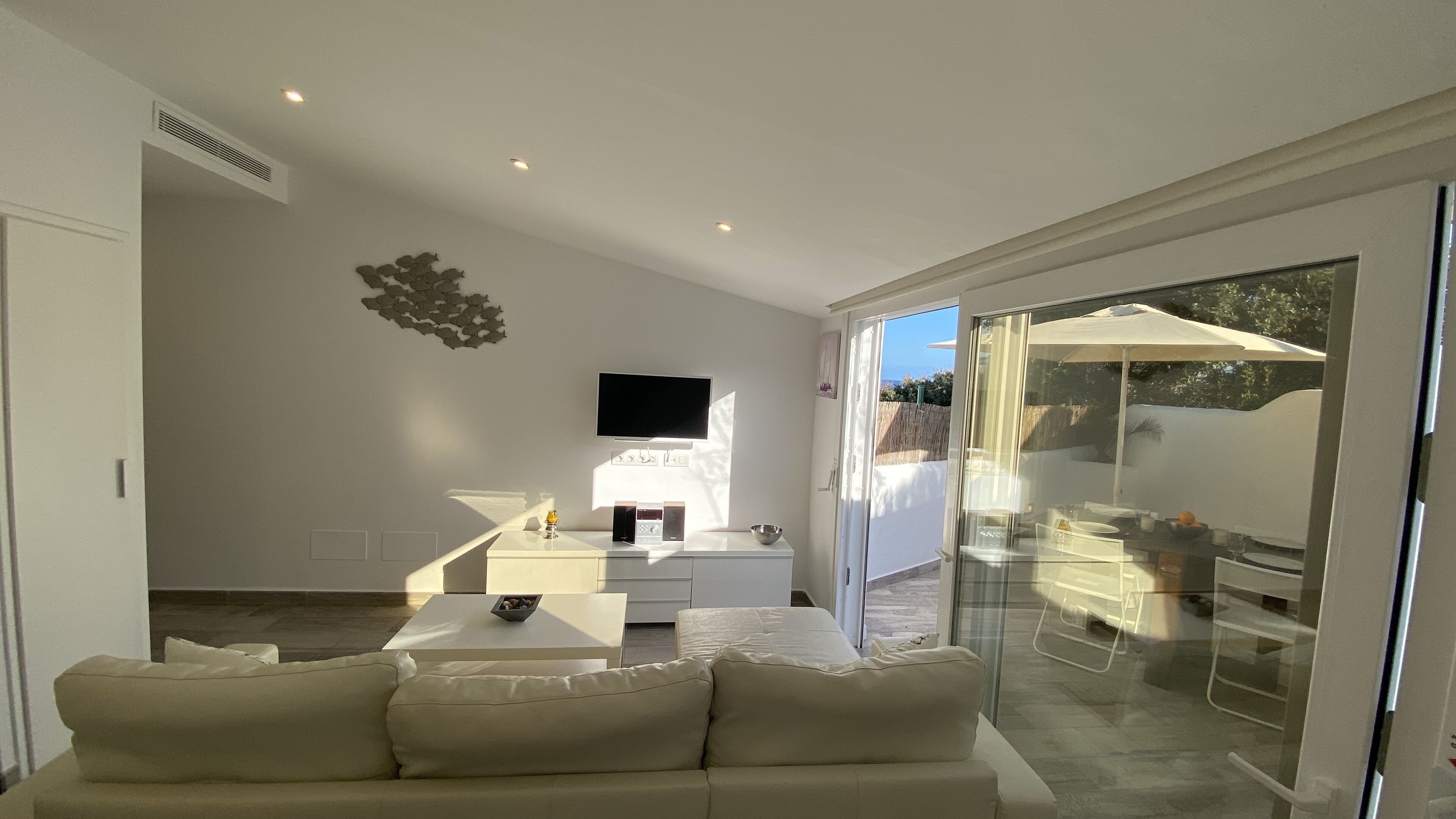 A modern living room with a sofa, a TV, and a glass door leading to an outdoor area.