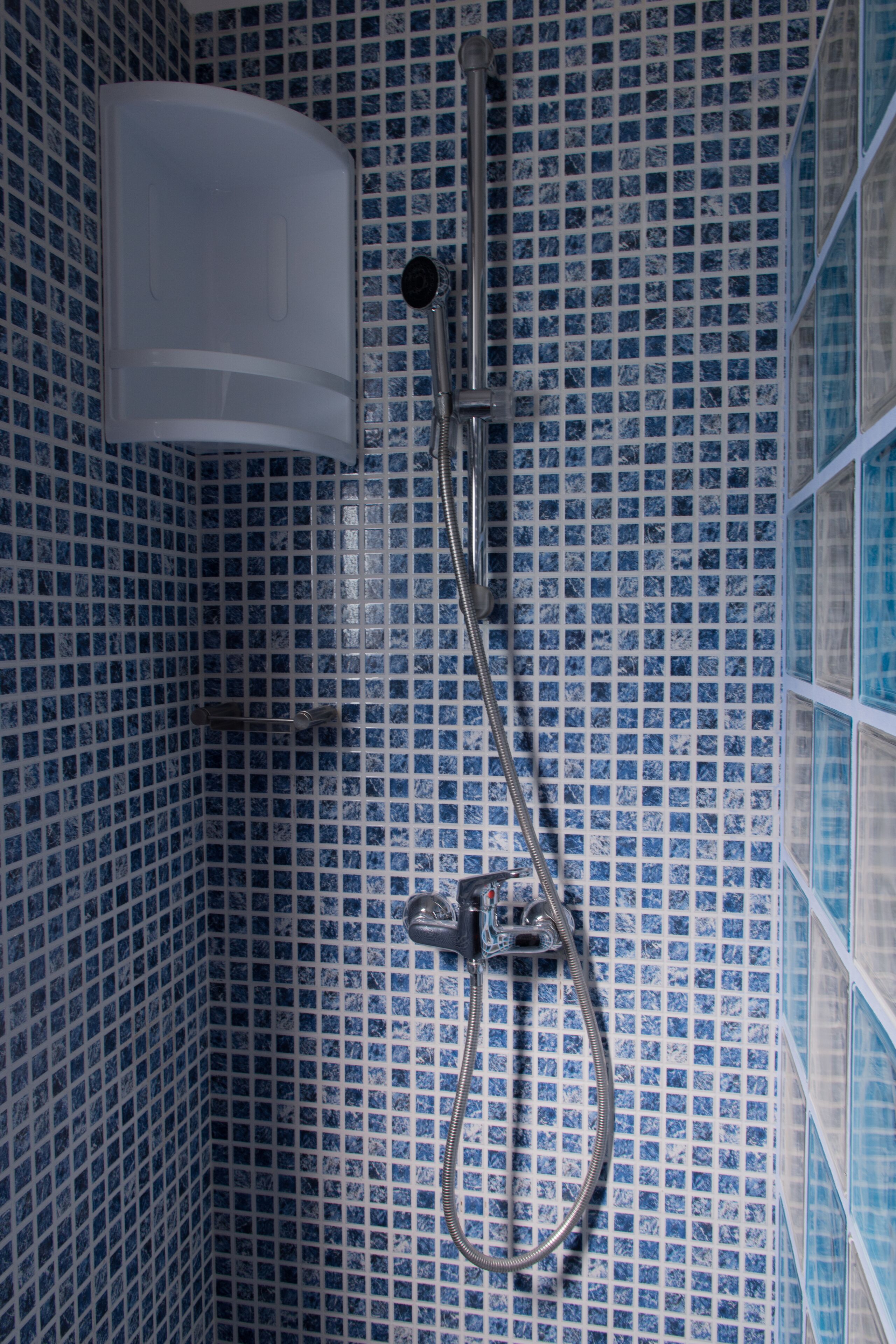 Une salle de bain avec des murs recouverts de carreaux bleus et une douche équipée d’un pommeau de douche à main et d’un robinet mural.