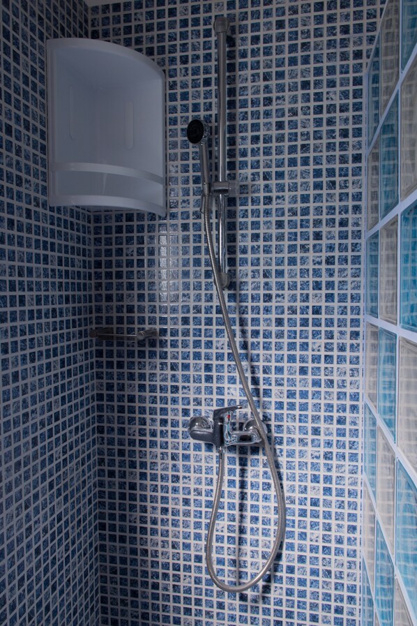 A bathroom with blue-tiled walls and a shower with a handheld showerhead and a wall-mounted faucet.