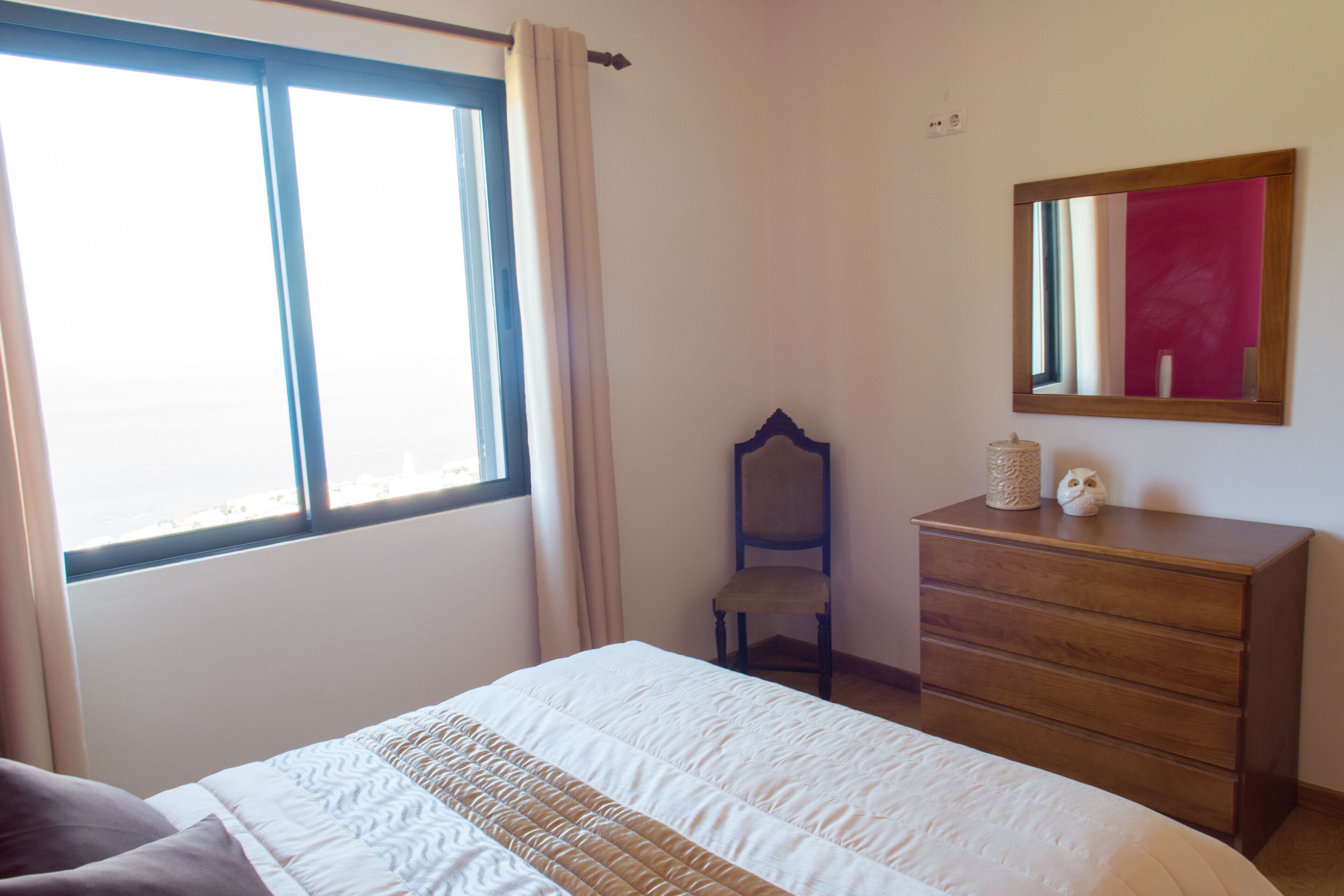 A bedroom with a bed, a dresser, a chair, and a window with curtains.