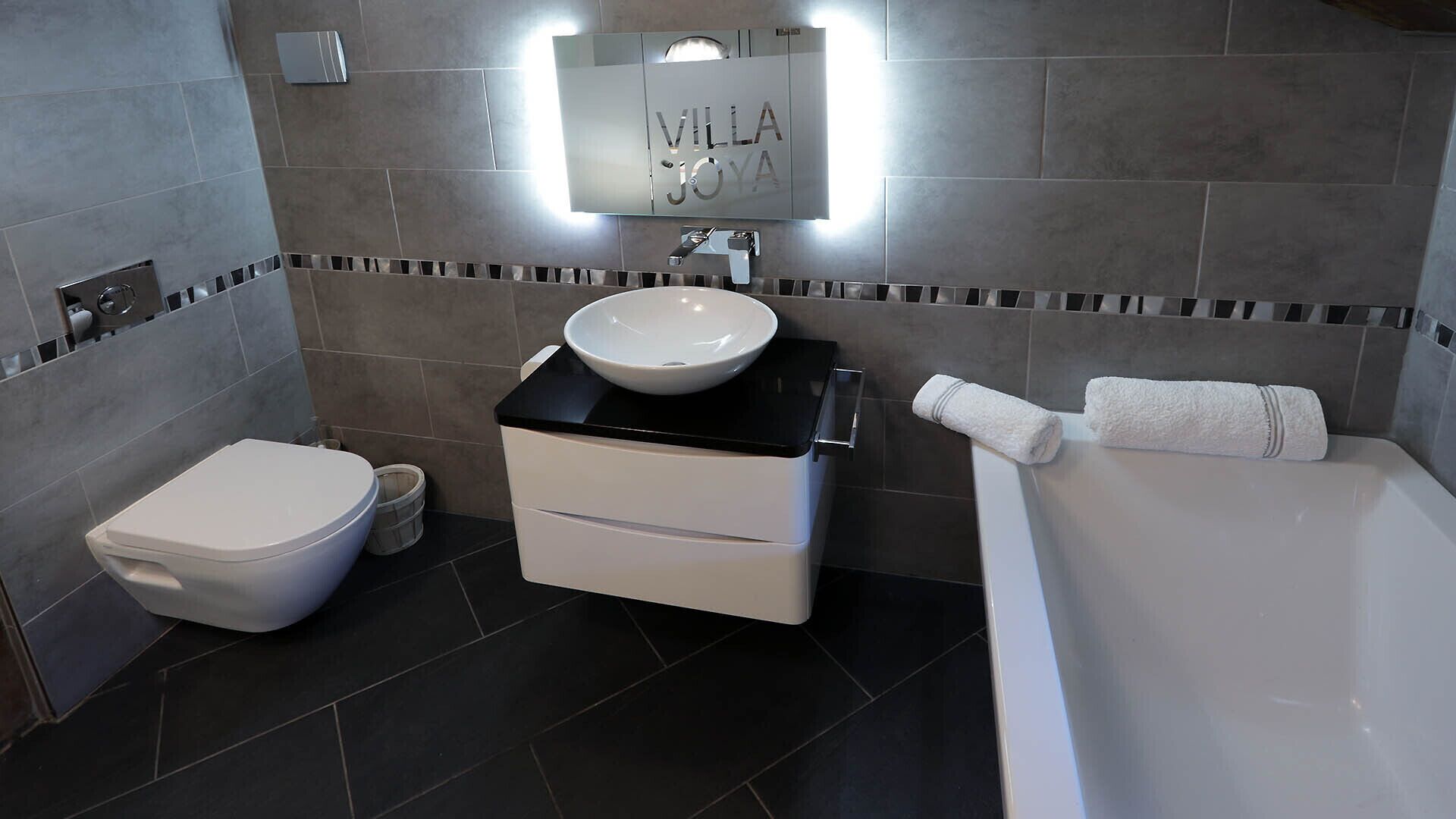 A modern bathroom with a white toilet, a sink with a black countertop, and a bathtub.
