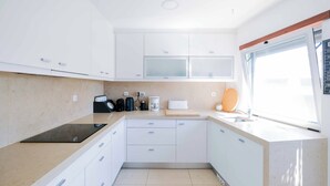 Una cocina moderna con armarios blancos, una placa de inducción negra, una cafetera y un ventanal que proporciona luz natural.