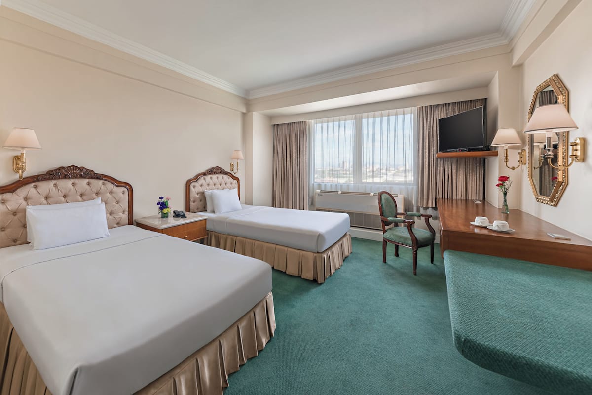 A hotel room with two beds, a desk, a chair, a TV, and a large window with curtains.