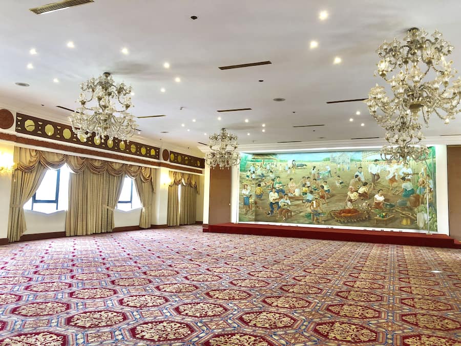 A spacious room with a patterned carpet, large windows with curtains, and a mural on the wall.