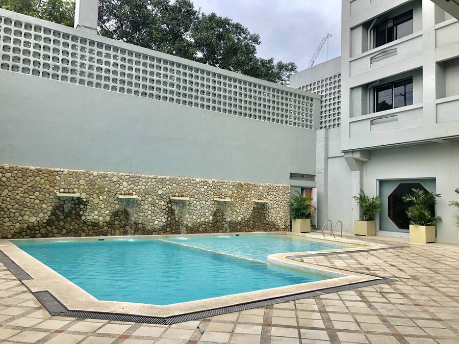 A swimming pool with a stone wall and a modern building in the background.