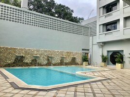 Piscina com muro de pedra e um edifício moderno ao fundo.