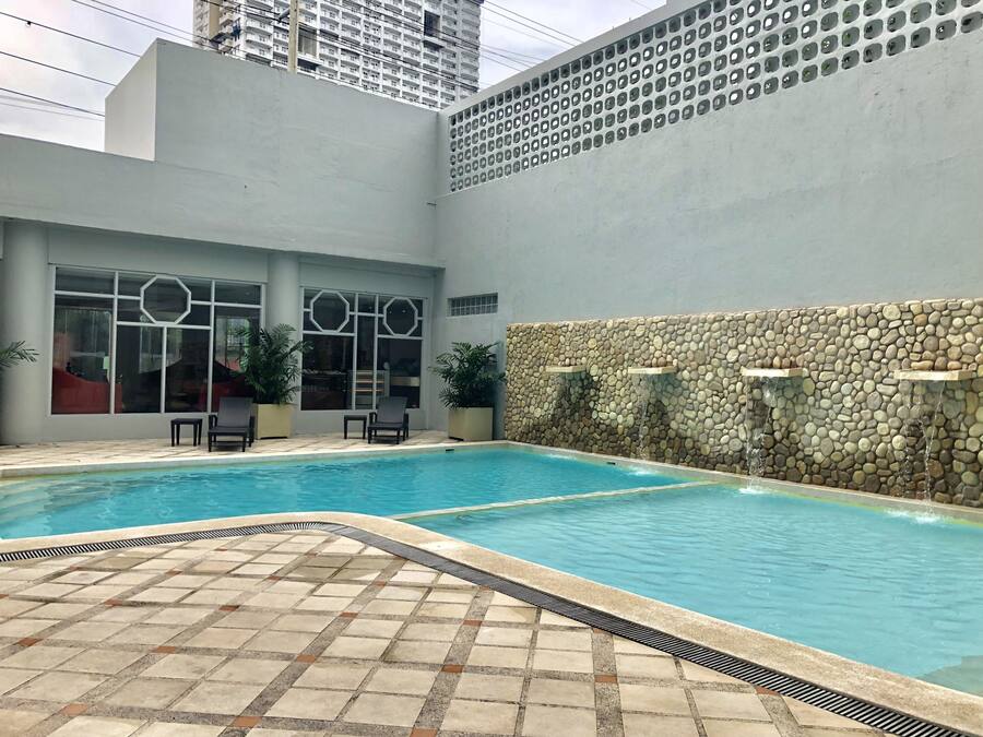 A swimming pool with a tiled deck, a stone wall with water features, and seating areas.