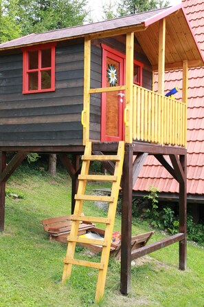 Una casetta in legno con una porta rossa e una scala gialla che conduce a un balcone.
