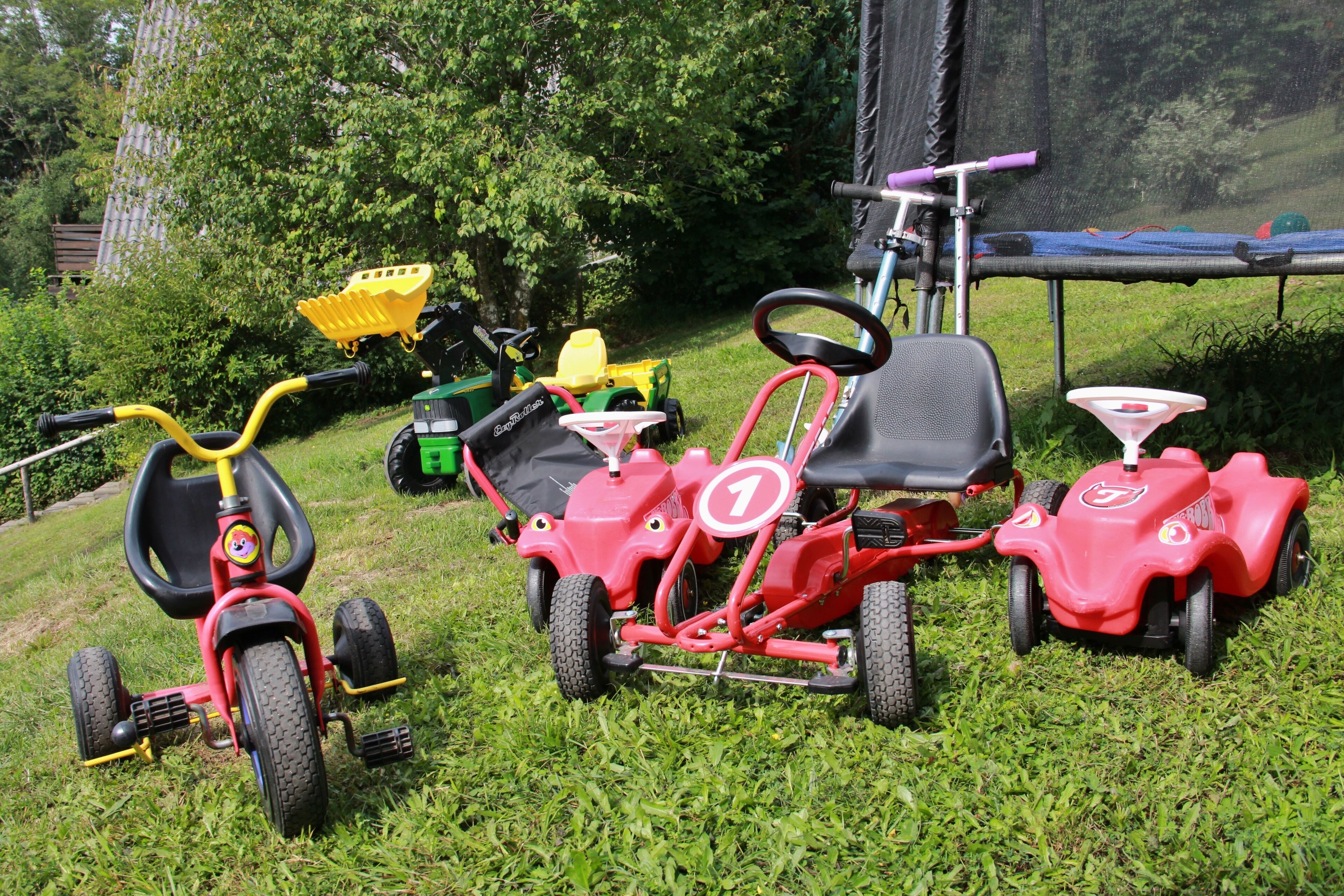 A grassy area with various children's tricycles and a scooter.