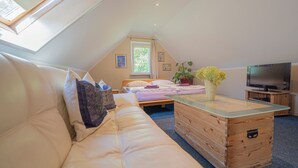 A cozy loft bedroom with a sloped ceiling, a large window, a bed, a wooden dresser, a TV, and a sofa. - Comfortable apartment with panoramic views of the Giant Mountains (Jezów Sudecki)