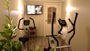 A home gym with two stationary bikes, a TV displaying workout metrics, and a door leading to another room. - Comfortable apartment with panoramic views of the Giant Mountains (Jezów Sudecki)