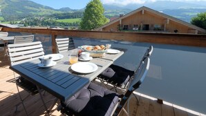 A dining area with a table set for two, a wooden deck, and a view of a mountain landscape.
