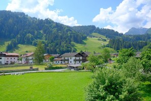 Un pueblo rural con casas tradicionales, un campo verde y colinas boscosas al fondo.