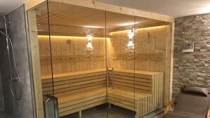 A sauna with wooden benches and glass walls, a stone wall, and a wooden bench outside.