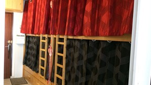 A room with a wooden wardrobe, a red curtain, and patterned curtains.