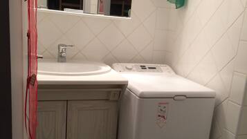 A compact bathroom with a white sink, a toilet, and a washing machine.
