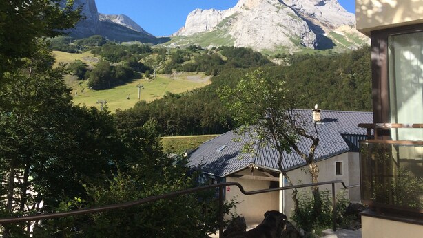 A mountain landscape with a prominent peak, a house with a sloped roof, and a balcony with a railing.