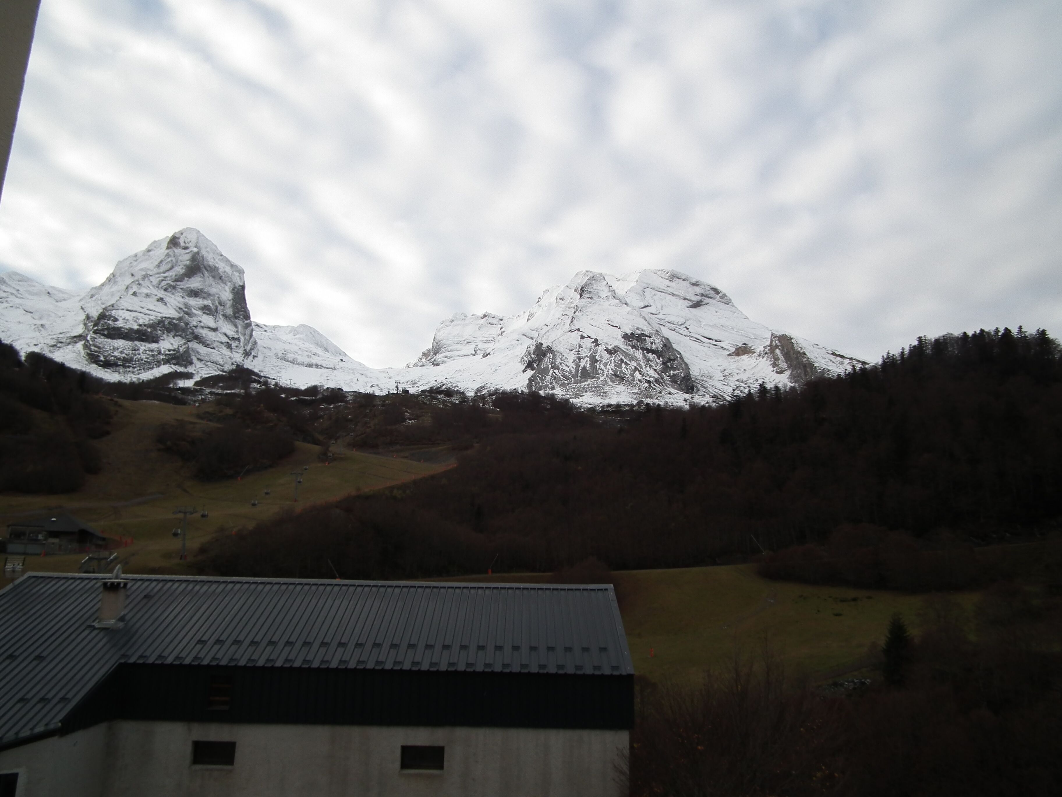 Un paysage de montagne avec des sommets enneigés et, au premier plan, un bâtiment doté d’un toit en métal.