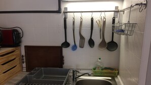 A kitchen with a stainless steel sink, a drying rack, and various kitchen utensils hanging on the wall.