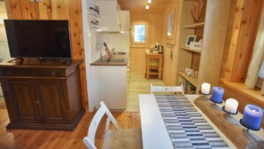 Ein Holzblockhaus-Interieur mit Fernseher, Esstisch mit Kerzen und Küchenbereich.
