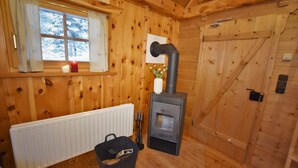 Ein Holzblockhaus-Interieur mit Kaminofen, Fenster mit Vorhängen, Heizkörper und einer Tür.