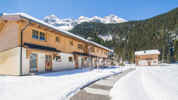 A wooden building with a snow-covered roof and a mountain backdrop.