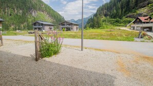A rural mountain road with houses on either side, a gravel path, and a street lamp.