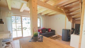 A spacious living area with a wooden ceiling, a sofa with red cushions, a small table with a plant, and a fireplace.