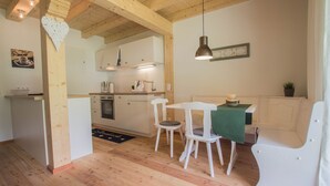A cozy kitchen with wooden beams, white cabinets, a dining area with a table and chairs, and a hanging pendant light.