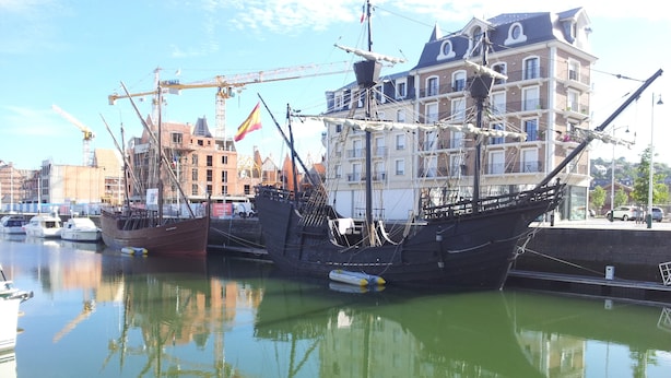 Ein historisches Schiff liegt im Hafen vor einer Gebäudereihe.