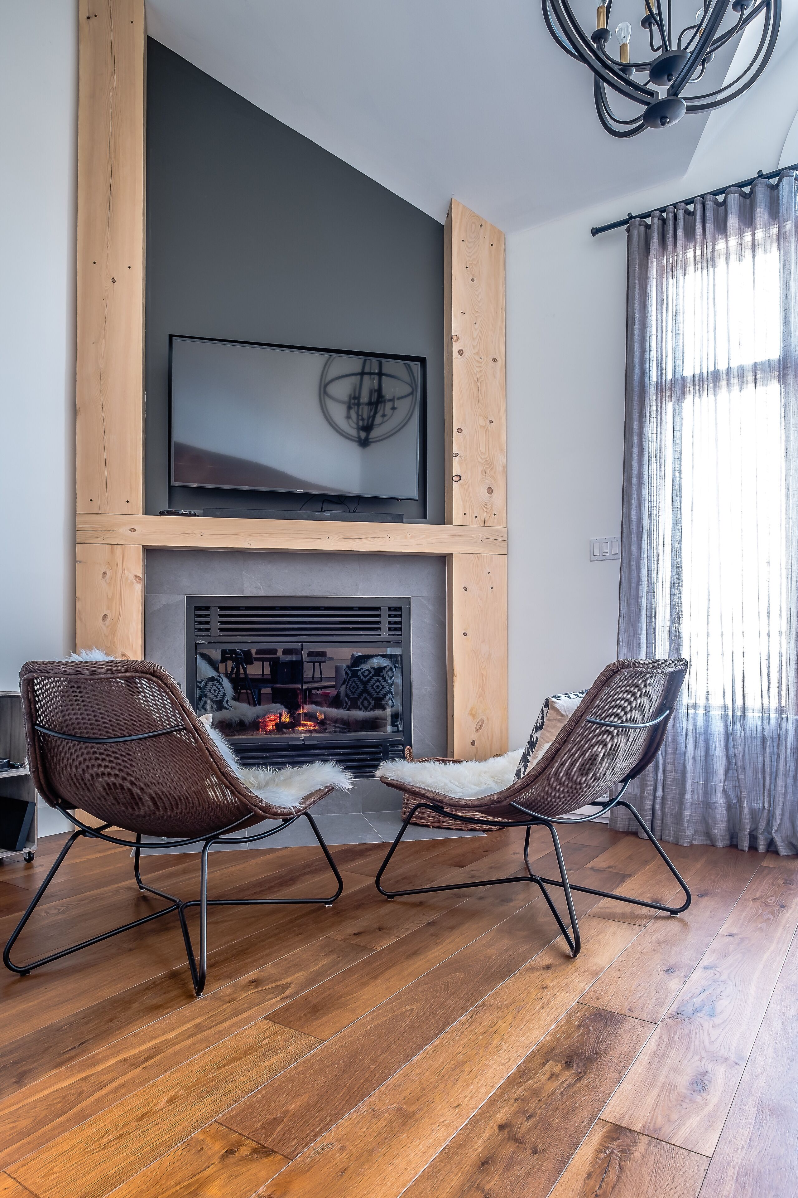 A living room with a fireplace, two chairs, a TV, and a wooden ceiling structure.