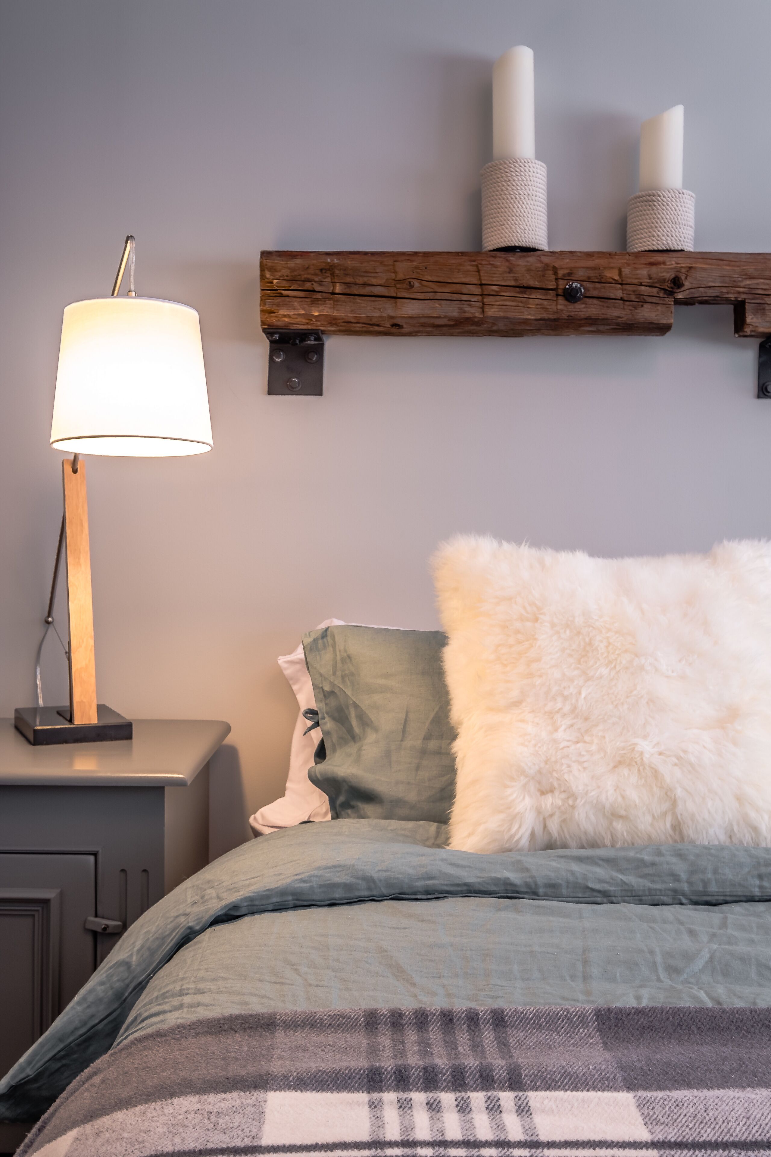 Une chambre à coucher avec un lit, une lampe de chevet, un oreiller moelleux, un oreiller vert et une étagère avec des bougies.