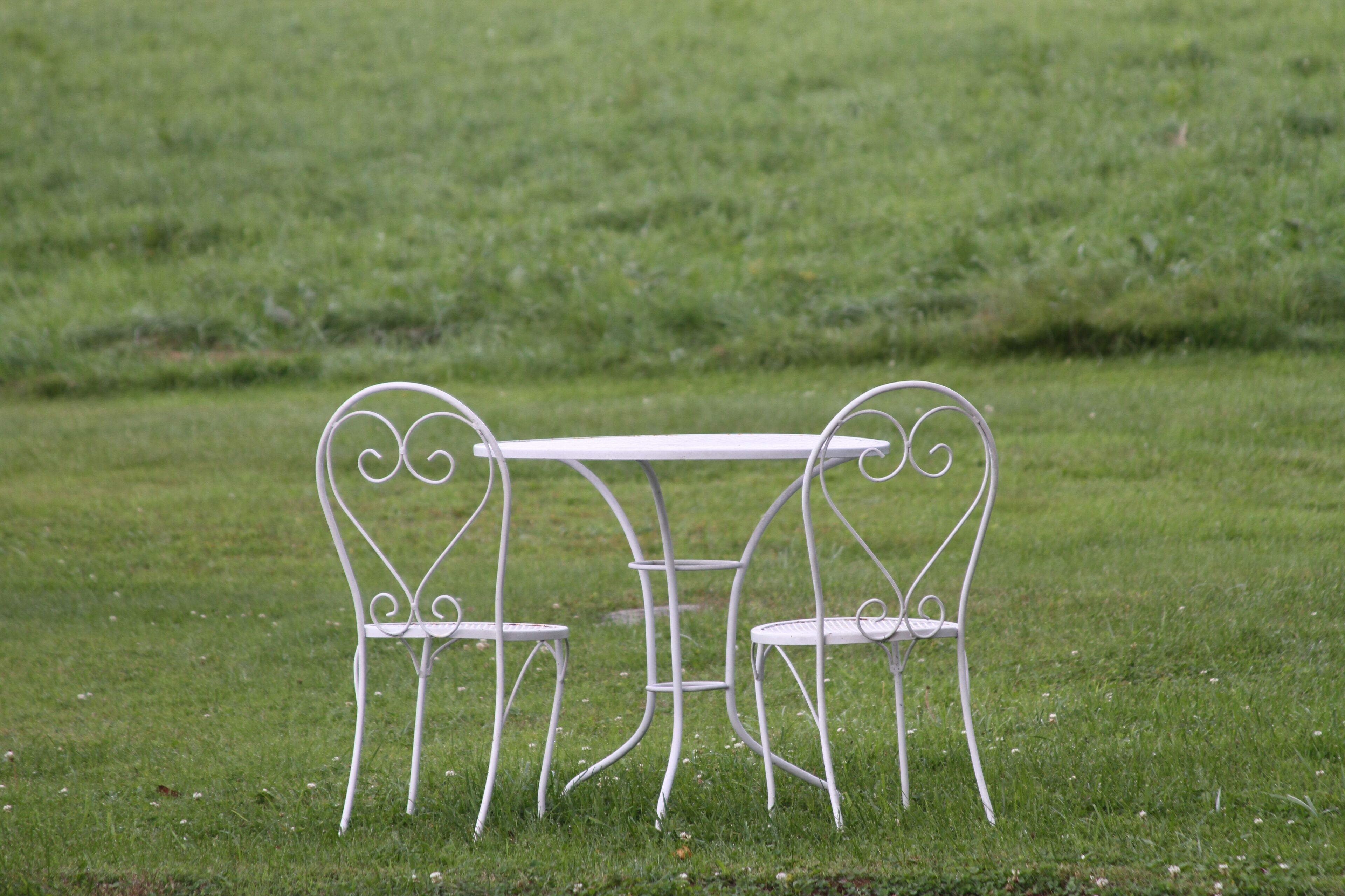 A white metal table and two chairs in a grassy field.