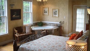Ein Schlafzimmer mit einem großen Bett, einer Sitzecke mit einem Sessel, einer Badewanne und einer Chandelier.