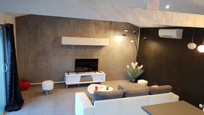 A modern living room with a white sofa, a coffee table, and a flat-screen TV mounted on the wall. - Charming apartment in Provence (Châteaurenard)