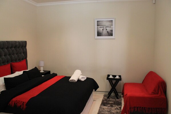A hotel room with a bed, a small table, a chair, and a framed picture on the wall.