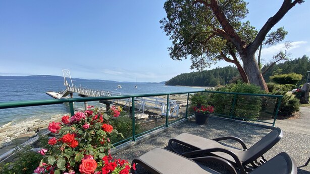 Terraza con sillones de descanso y barandilla con vista a un cuerpo de agua y barcos.
