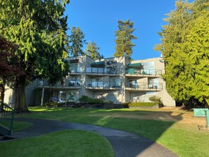A multi-story residential building with balconies, a paved driveway, and surrounding greenery.