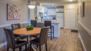 Una cocina moderna con armarios blancos, una isla central y un comedor con mesa de madera y sillas de cuero.