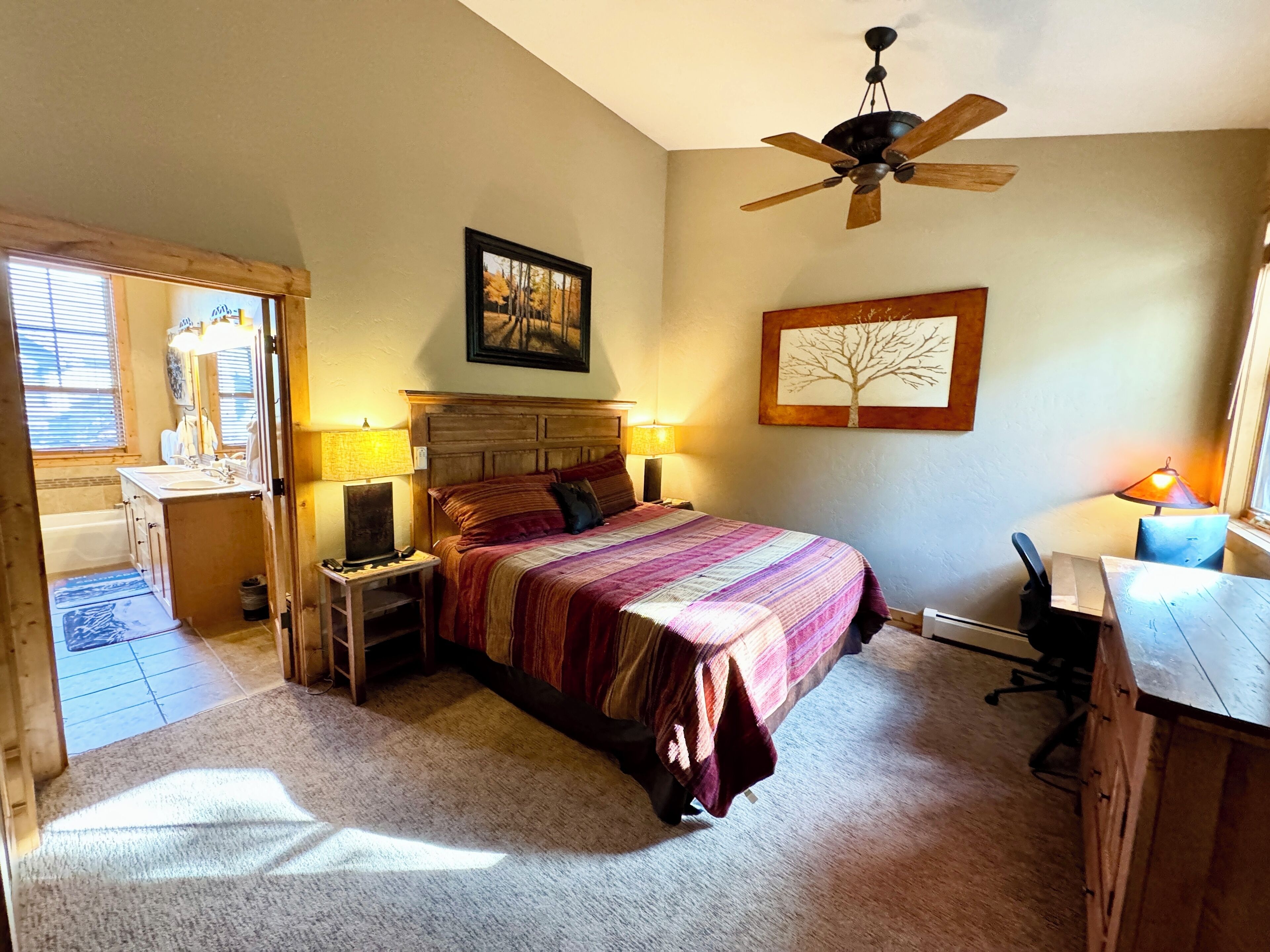 A bedroom with a bed, bedside tables, a desk, a ceiling fan, and a window.